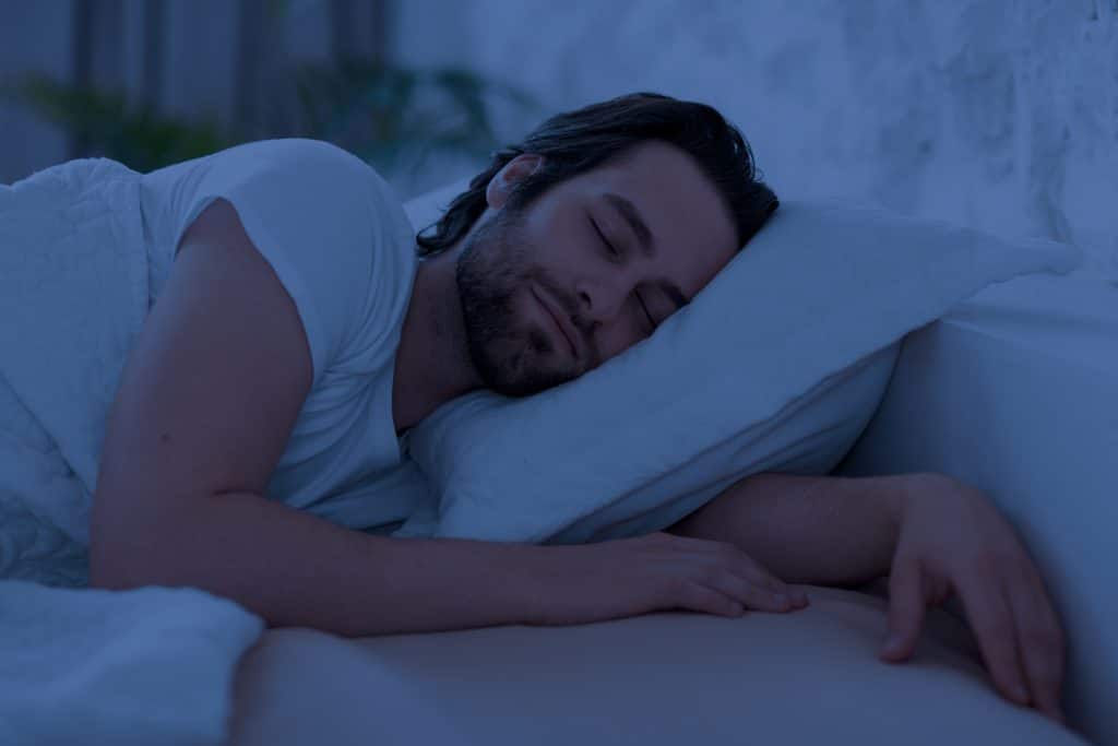 Joven tranquilo durmiendo en la cama por la noche. Destaca la importancia del sue帽o de calidad para la regulaci贸n hormonal y la fertilidad masculina.