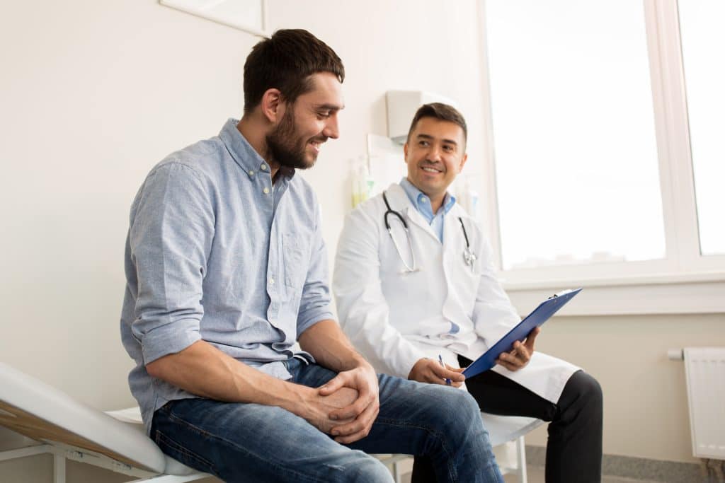 Un médico sonríe y habla con un joven durante un chequeo médico, promoviendo la concienciación sobre la salud masculina y la comunicación abierta.